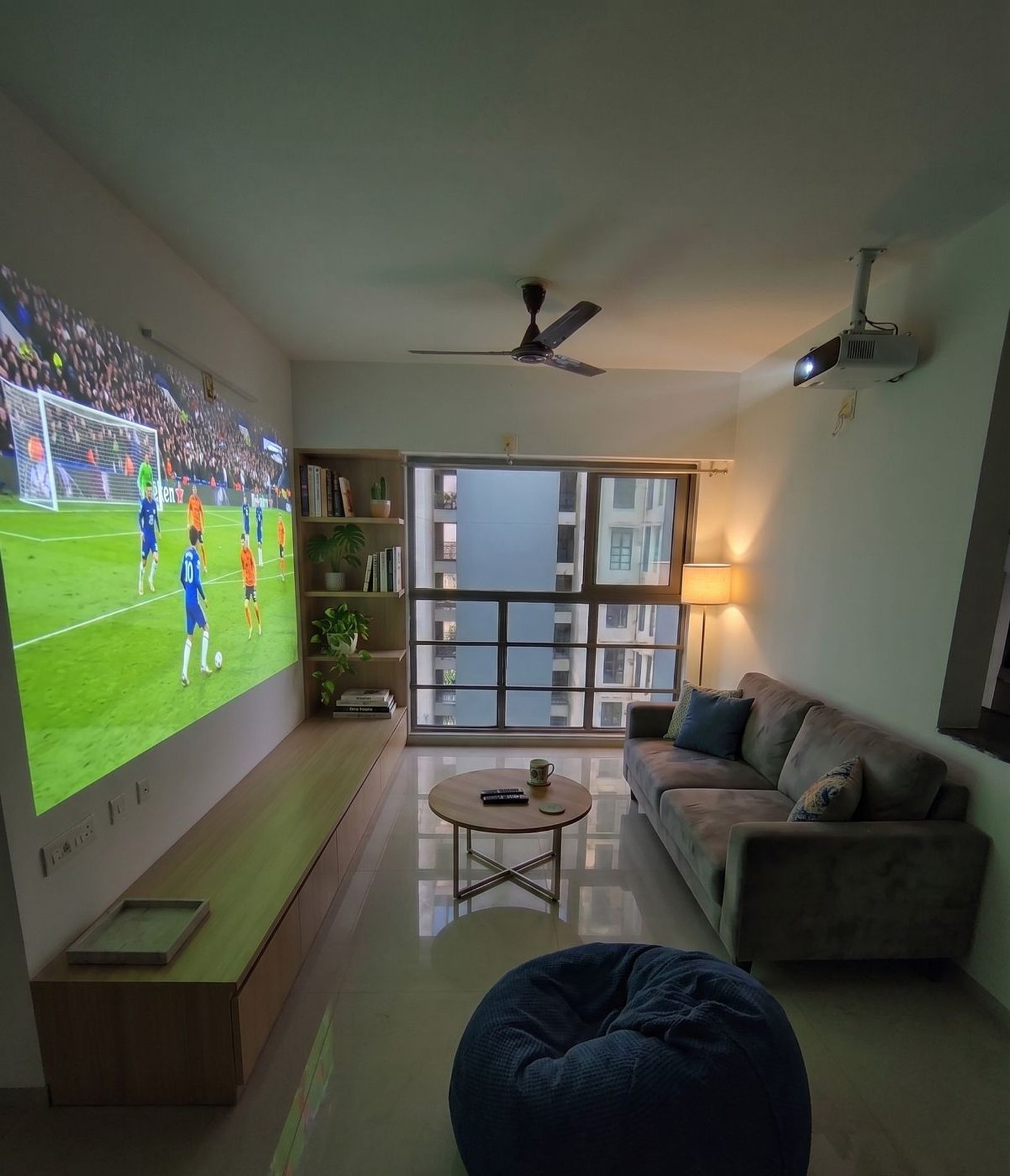 A Halapeno Homes living room at night — projector on, sofa, bean bag and a wall of books